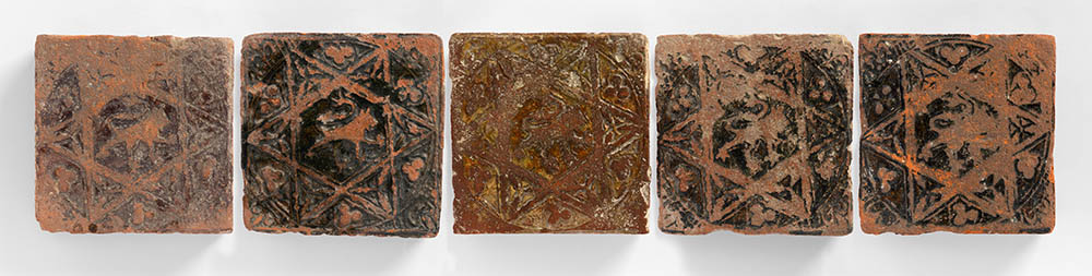 Five tiles in a line showing different colours and states of wear. The design is a Lion rampant in a Star of David, the arms of Hugh Bigod.